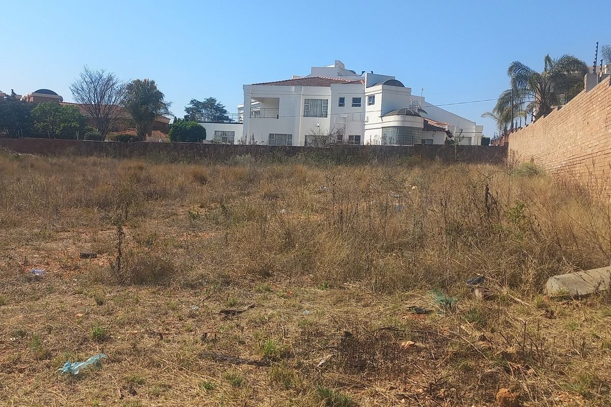 A vacant residential plot featuring a perimeter brick wall with electric fencing, currently covered in dry, overgrown vegetation.