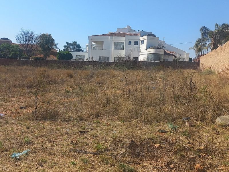 A vacant residential plot featuring a perimeter brick wall with electric fencing, currently covered in dry, overgrown vegetation.
