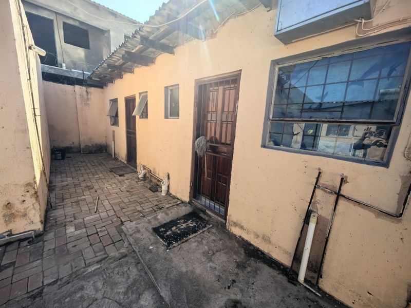 Rear exterior courtyard featuring paved flooring, security gates, and steel-framed windows, showing significant signs of wear and maintenance requirements.