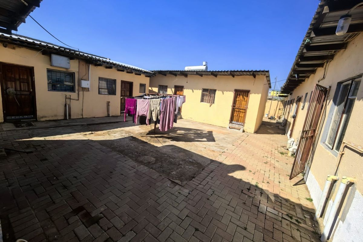 A paved rear courtyard area featuring multiple building access points, corrugated roofing, and a solar water heating system.