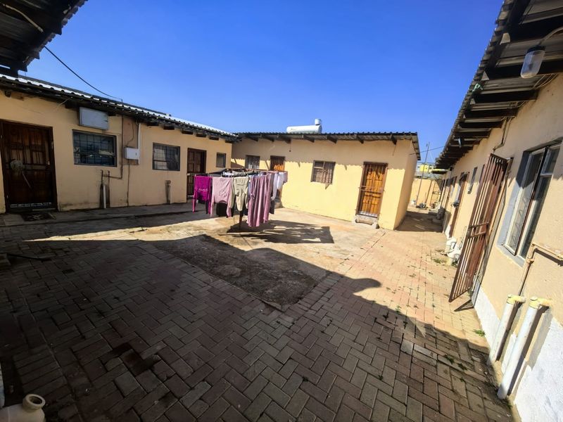 A paved rear courtyard area featuring multiple building access points, corrugated roofing, and a solar water heating system.