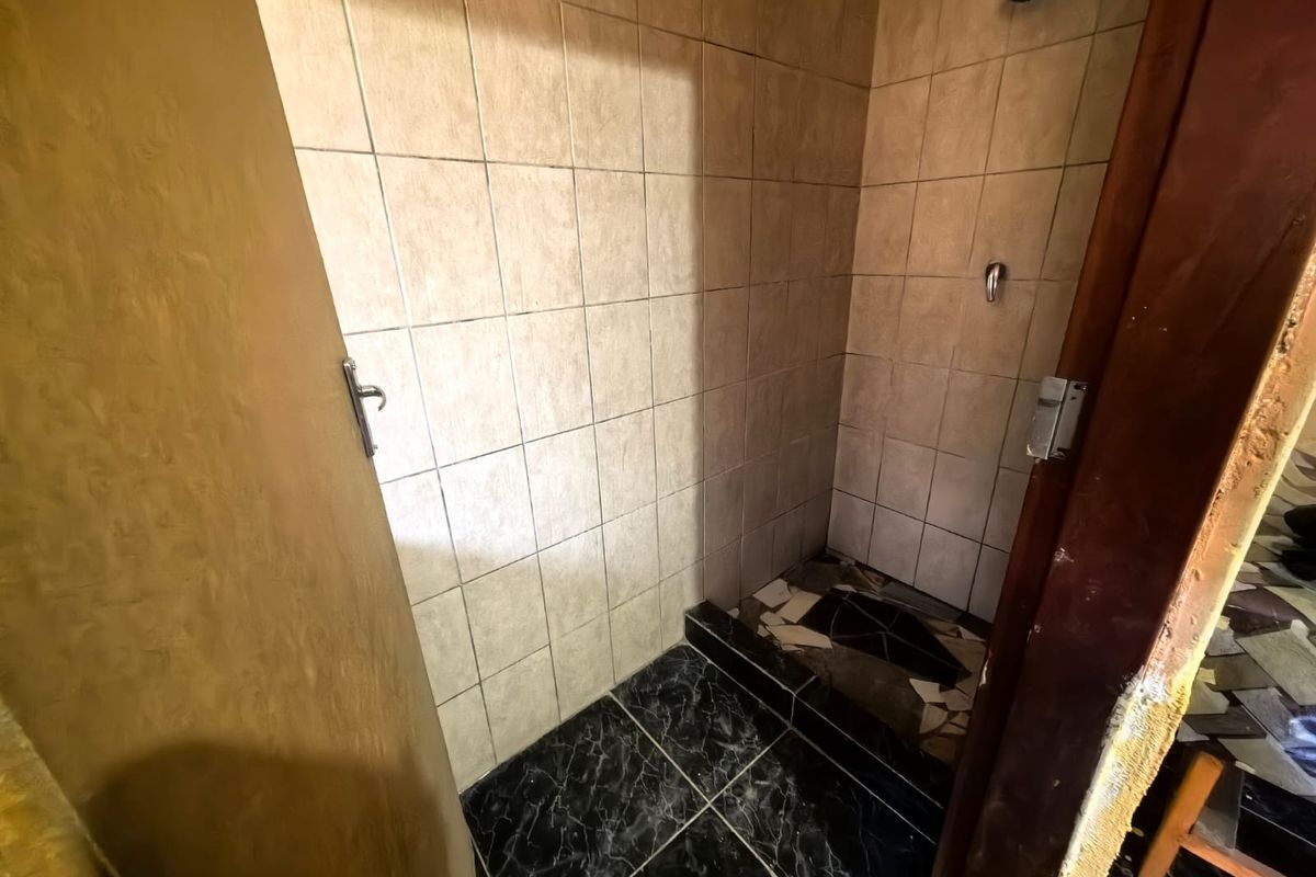A small shower enclosure featuring tiled walls and flooring, currently showing signs of wear and damage to the floor tiles and door frame.