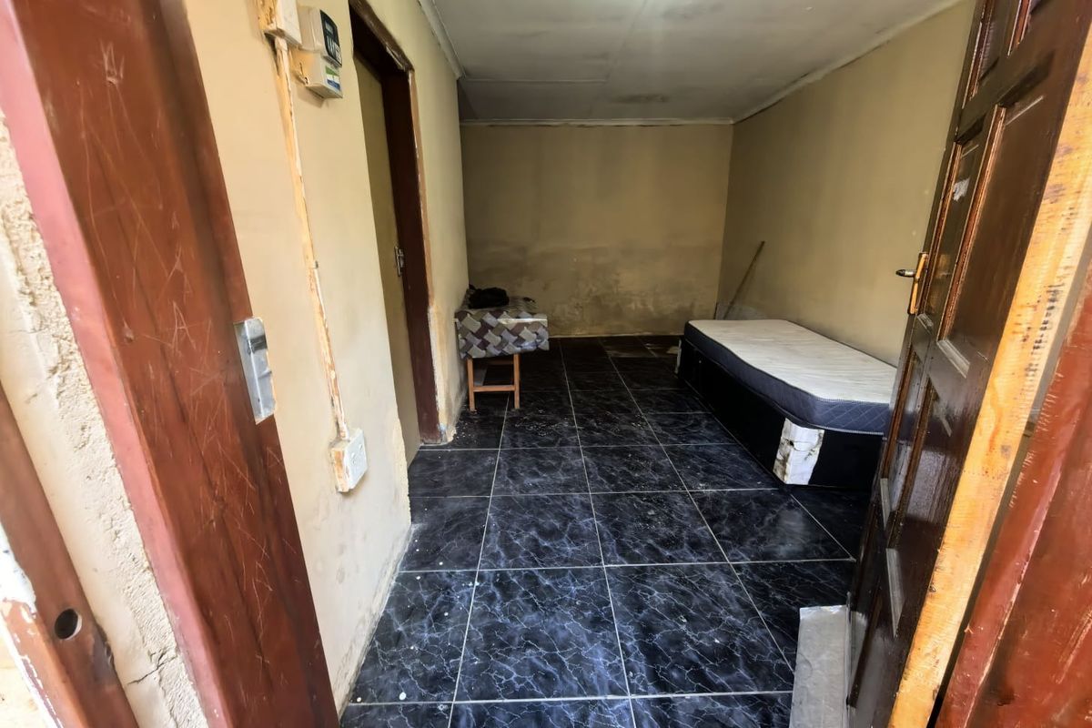 A small bedroom featuring dark tiled flooring and plain walls, currently requiring maintenance and cosmetic updates to improve the overall condition.