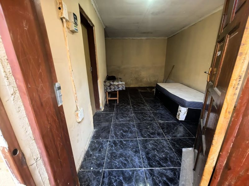 A small bedroom featuring dark tiled flooring and plain walls, currently requiring maintenance and cosmetic updates to improve the overall condition.