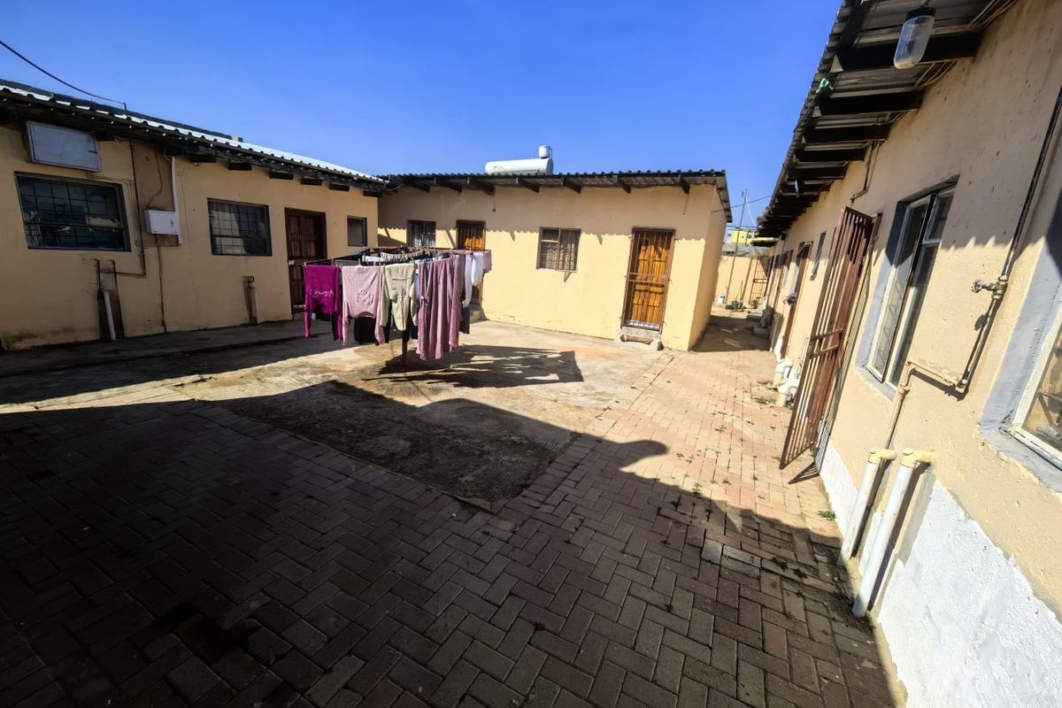 A paved rear courtyard area featuring multiple building access points, security gates, and a solar geyser installation.