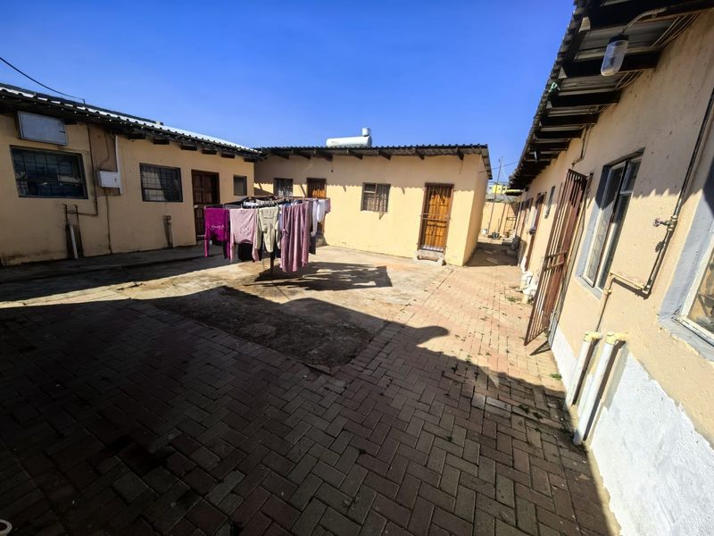 A paved rear courtyard area featuring multiple building access points, security gates, and a solar geyser installation.
