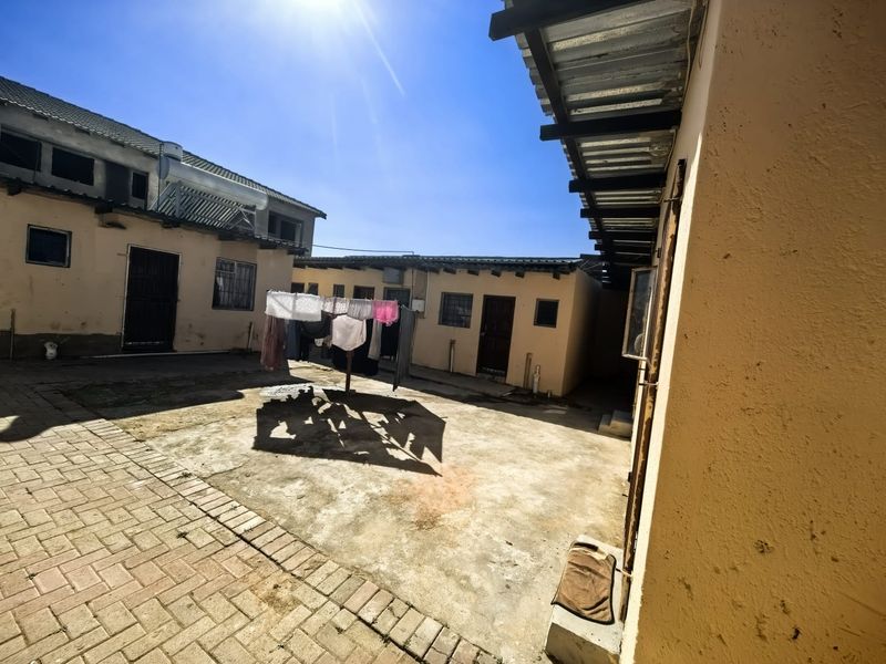 A rear courtyard area featuring paved surfaces, corrugated roof overhangs, and multiple building access points with security gates.