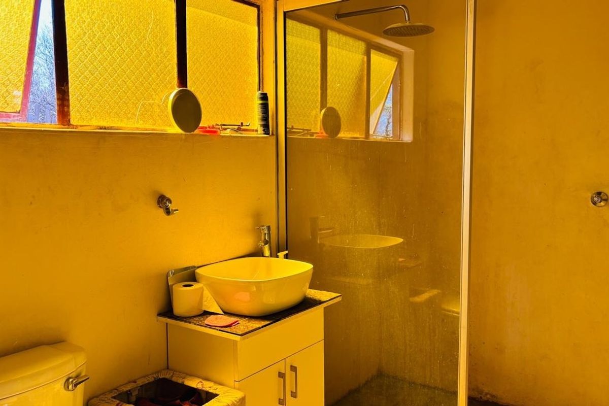 A bathroom featuring a vessel sink on a vanity cabinet, a glass-enclosed shower with a rain shower head, and a standard toilet.