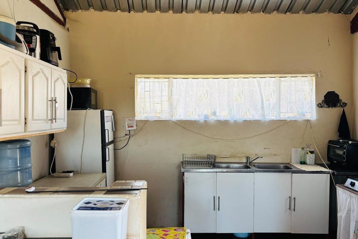 A functional kitchen area featuring built-in cabinetry, a double sink, and a corrugated metal ceiling, requiring cosmetic updates to improve its overall condition.