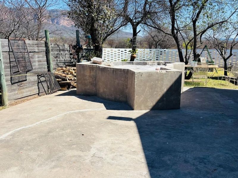 Outdoor patio area featuring a large concrete braai, concrete flooring, and perimeter fencing, set within a rural farm landscape.