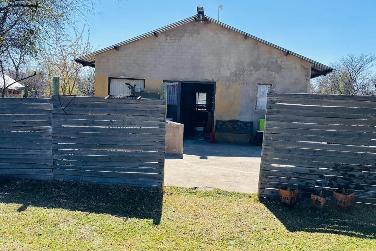 Rear view of a farm dwelling featuring a concrete patio area enclosed by timber slat fencing and a weathered exterior facade.