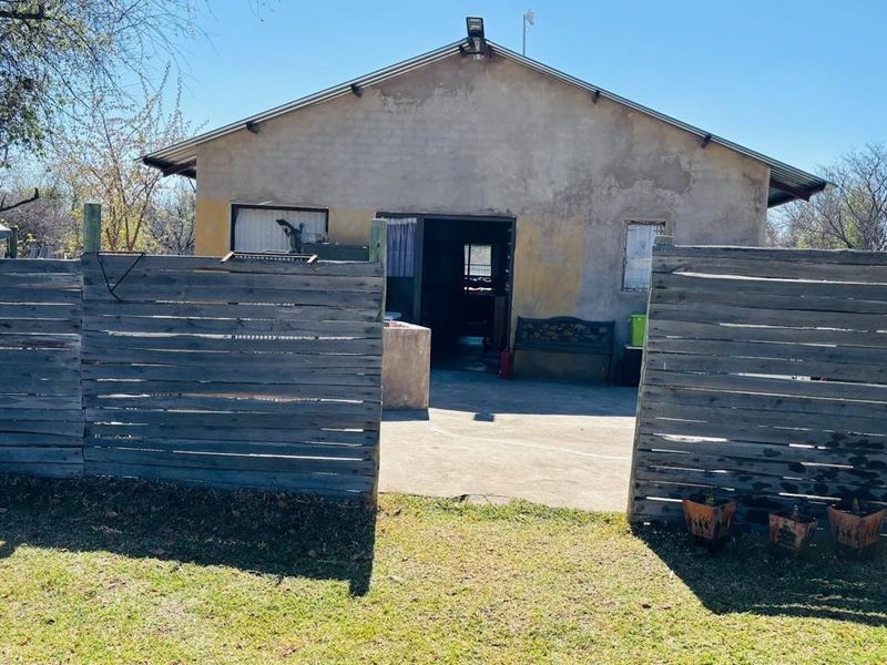 Rear view of a farm dwelling featuring a concrete patio area enclosed by timber slat fencing and a weathered exterior facade.