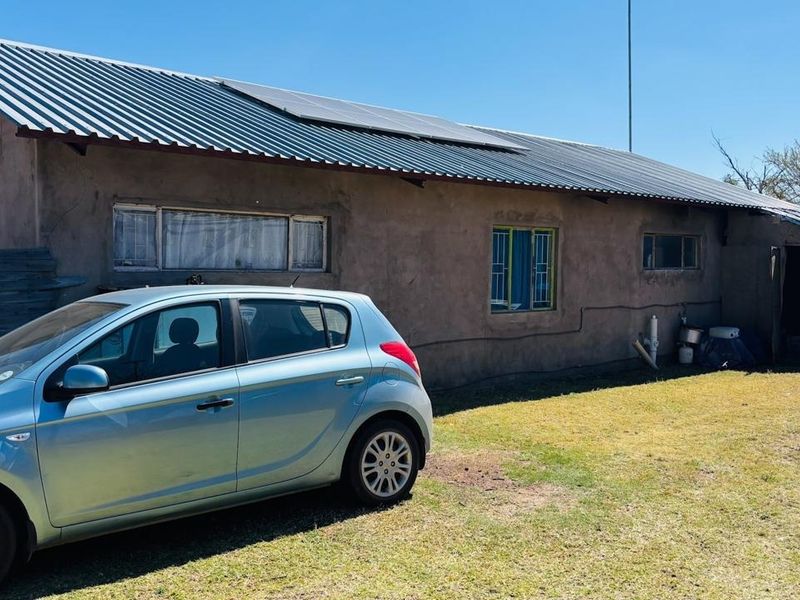Rear view of a farm dwelling featuring a corrugated metal roof with installed solar panels and plastered masonry walls.