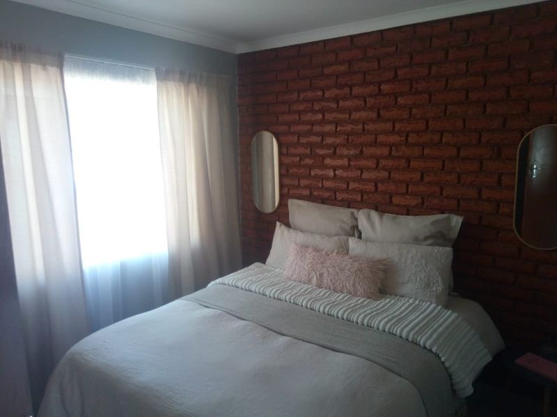 A cozy bedroom featuring a prominent exposed red brick feature wall and neutral finishes, creating a warm and inviting atmosphere.
