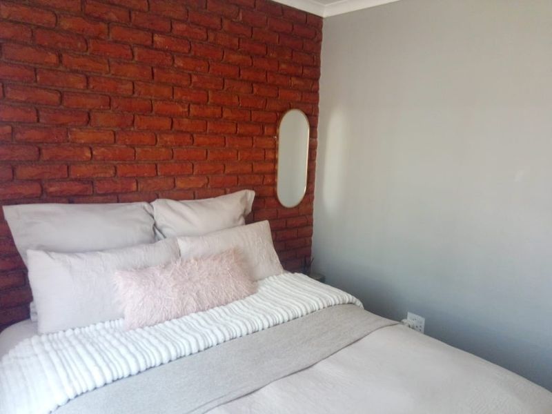 A cozy bedroom featuring a prominent exposed red brick feature wall and neutral painted walls.