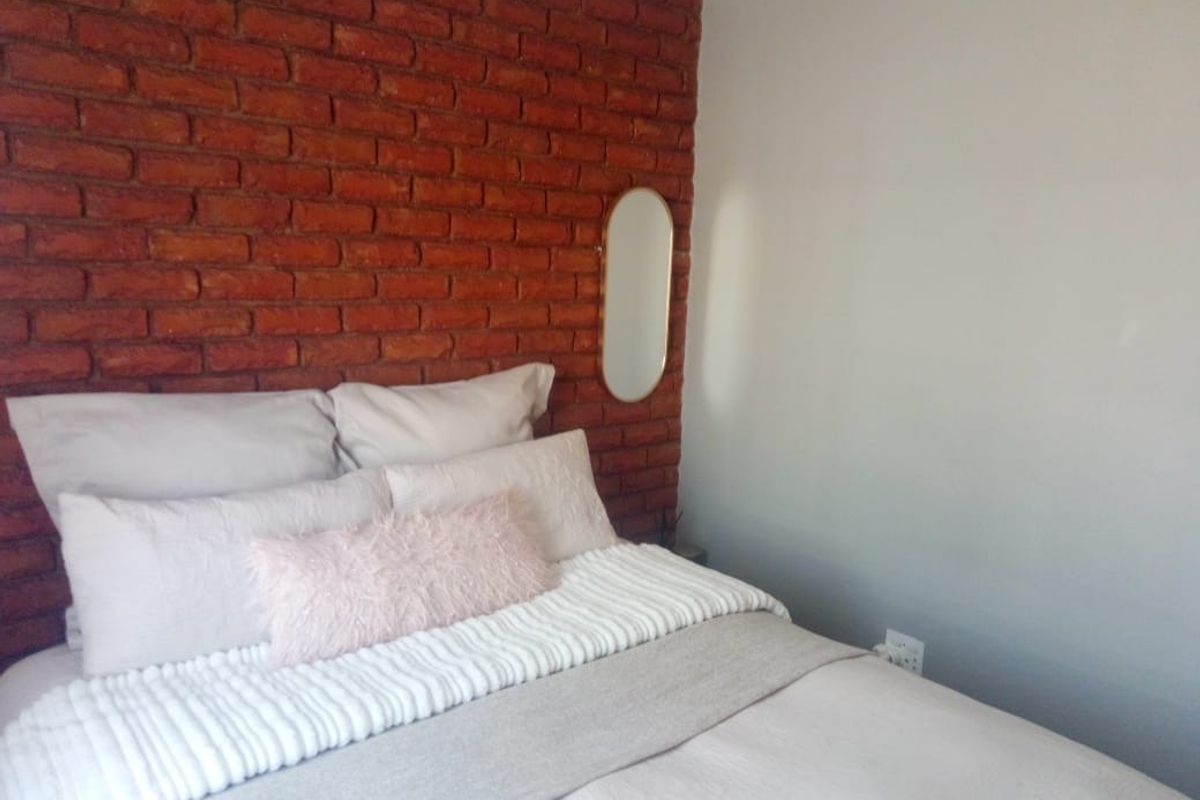 A cozy bedroom featuring a prominent exposed red brick feature wall and neutral painted walls.