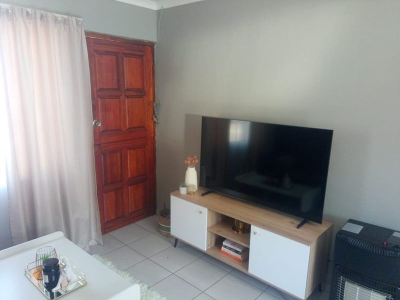 A living room area featuring tiled flooring and a traditional wooden door, with neutral wall paint and visible cable management.