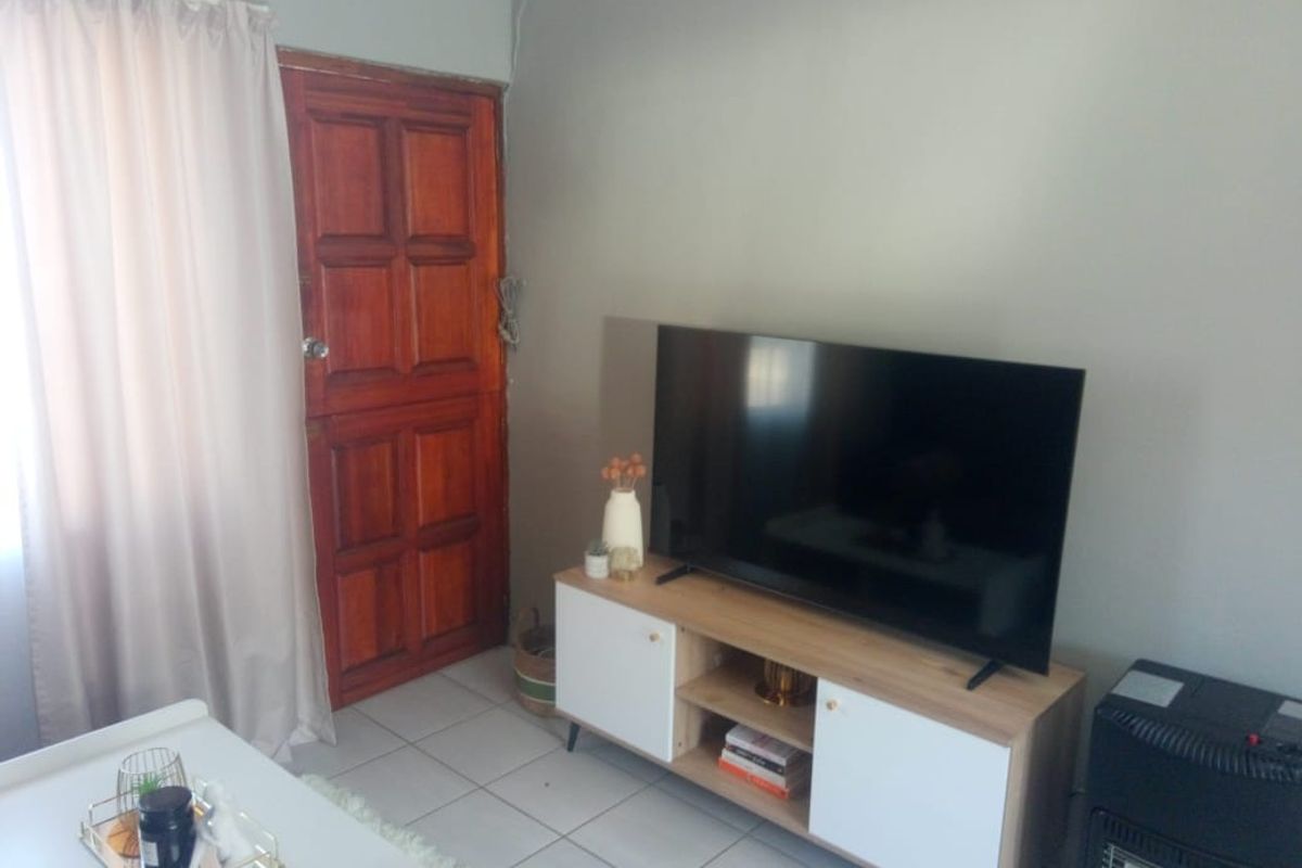 A living room area featuring tiled flooring and a traditional wooden door, with neutral wall paint and visible cable management.