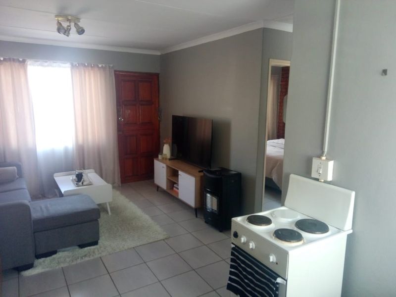 Open-plan living area featuring tiled flooring, a compact kitchen zone with an electric stove, and direct access to the main entrance.