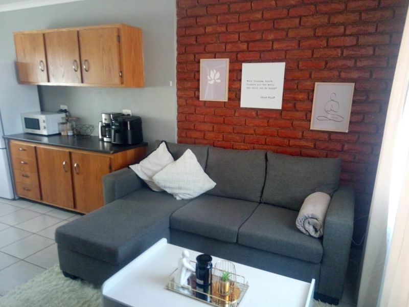 Open plan living area featuring a prominent exposed brick feature wall and adjacent kitchen cabinetry with laminate countertops and tiled flooring.