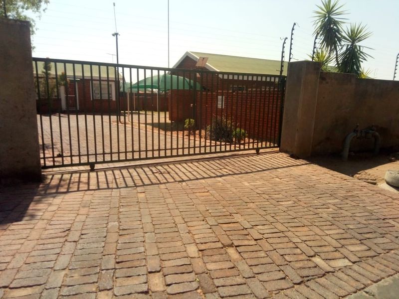 Front entrance view featuring a metal sliding gate, brick paved driveway, and perimeter wall with electric fencing.