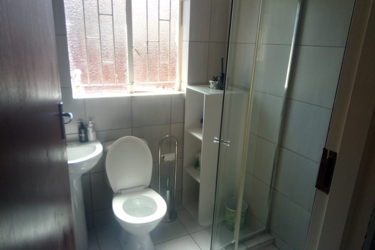 A functional bathroom featuring a pedestal basin, toilet, and a glass-enclosed shower with tiled finishes and a window for natural light.