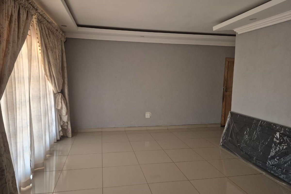 A spacious, empty living area featuring neutral tiled flooring, recessed ceiling details with cove lighting, and large sliding doors with curtains.