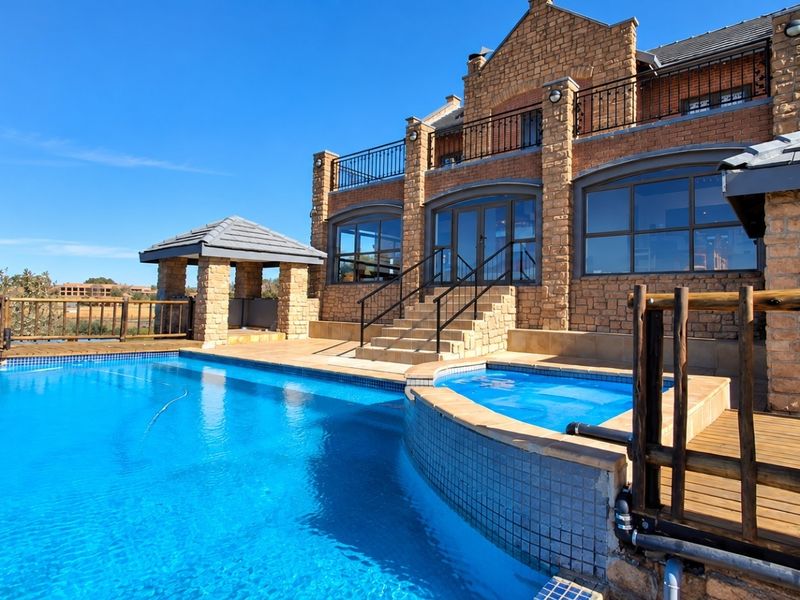 A well-maintained outdoor pool area featuring a raised spa, stone-clad facade, balcony, and a gazebo, set against a beautiful architectural backdrop.