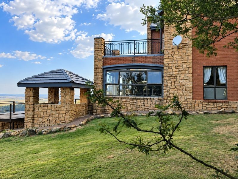 Rear view of a multi-level home featuring stone and brick masonry, a raised timber deck, and a stone gazebo overlooking a scenic landscape.