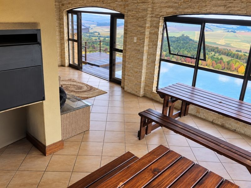 Spacious covered patio featuring stone-clad walls, a built-in fireplace, tiled flooring, and expansive windows offering panoramic landscape views with direct access to a deck.