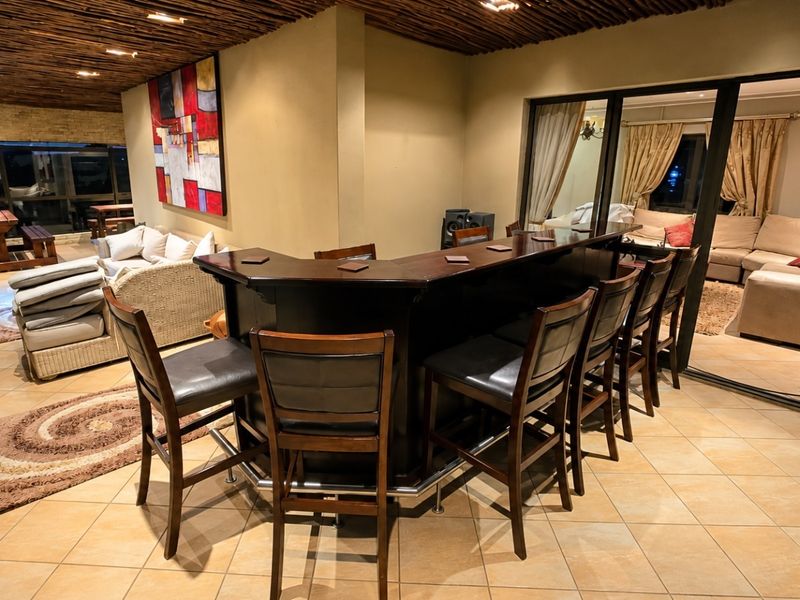 A spacious indoor bar area featuring a built-in counter, tiled flooring, and a unique timber slat ceiling, seamlessly connected to the adjacent living space.