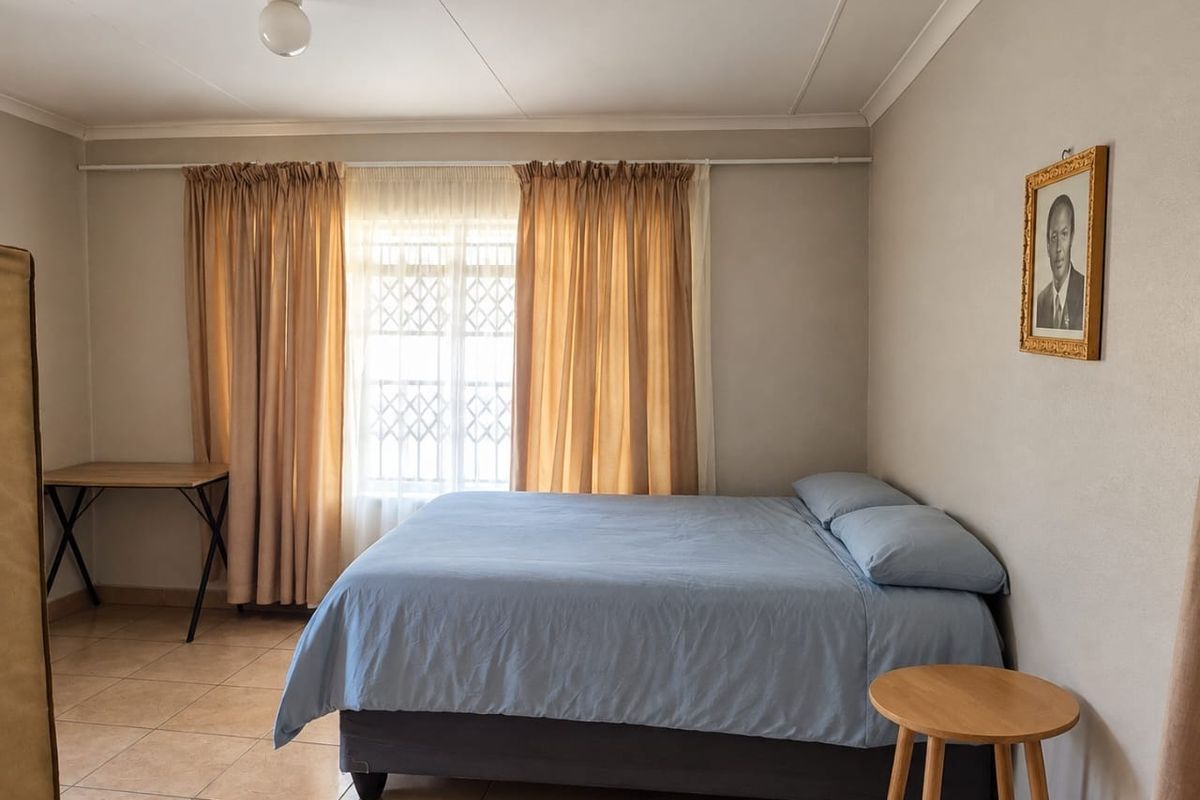 A functional bedroom featuring tiled flooring, security window bars, and neutral wall finishes, providing a clean and simple living space.