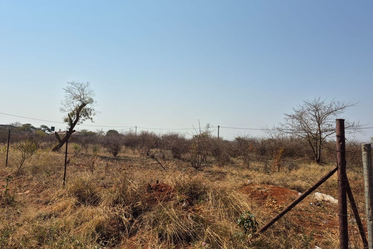 A view of a vacant residential plot featuring dry, overgrown vegetation and existing wire perimeter fencing.