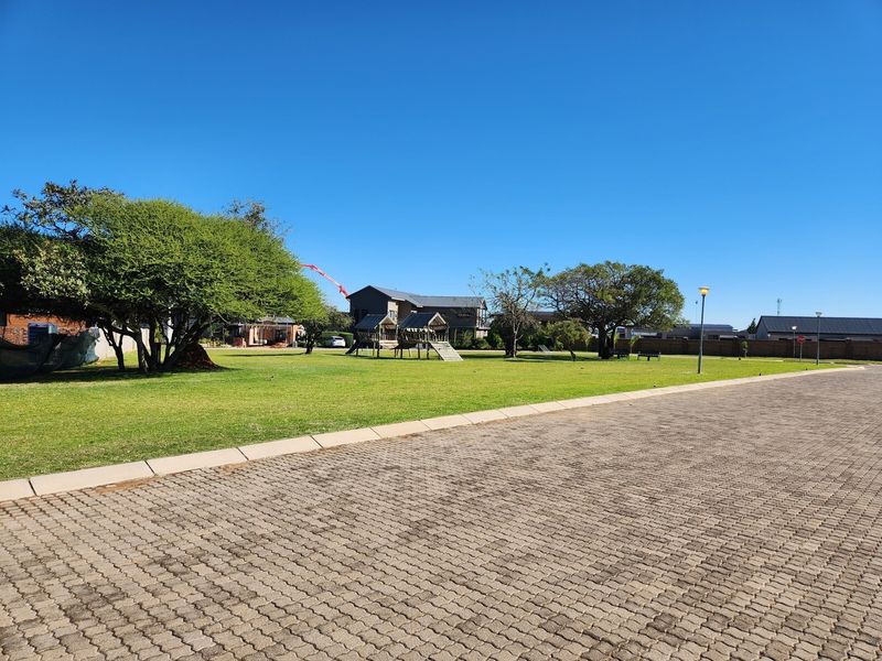 A well-maintained residential garden area featuring a paved driveway, expansive lawn, and mature trees in a quiet neighborhood setting.