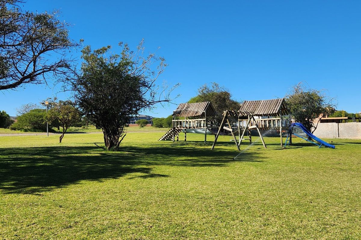 A spacious residential garden featuring a well-maintained lawn, mature trees, and a wooden playground structure with a slide.