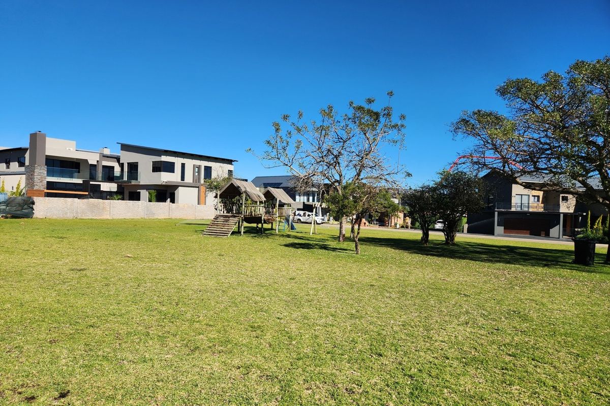 A spacious, well-maintained residential garden featuring a manicured lawn, mature trees, and a secure perimeter wall in a quiet neighborhood setting.