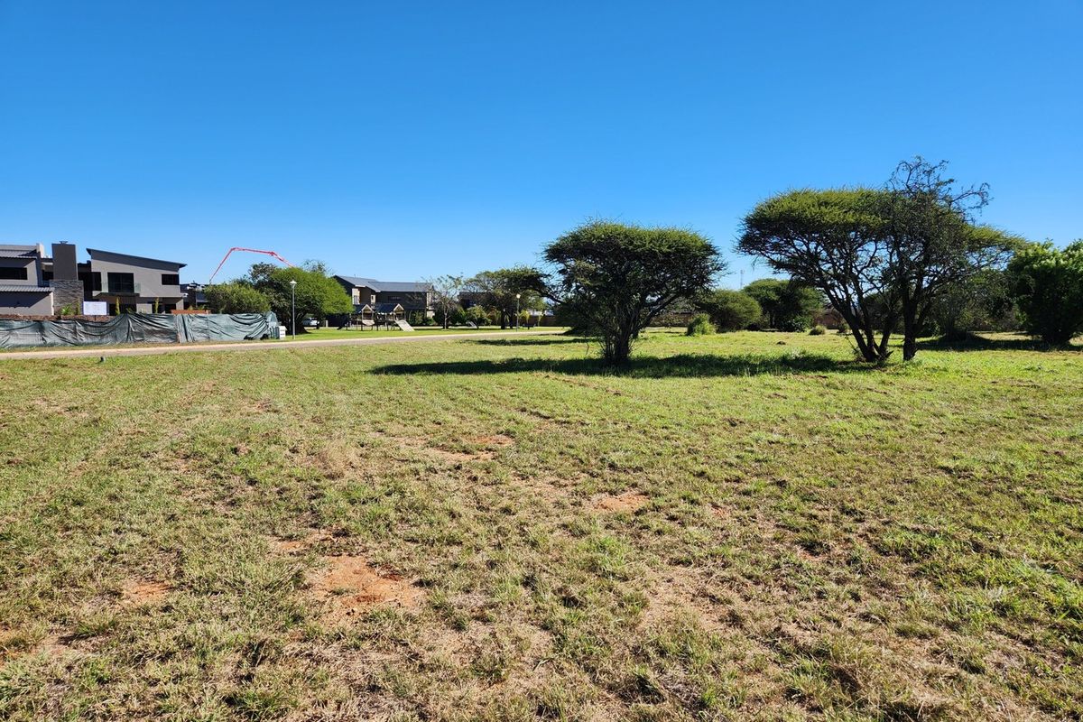 A vacant residential plot featuring open grassland and mature trees, situated in a developed neighborhood setting.
