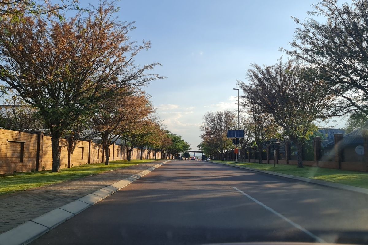 A view of a well-maintained residential street featuring paved roads, sidewalks, and established brick boundary walls within a secure estate setting.
