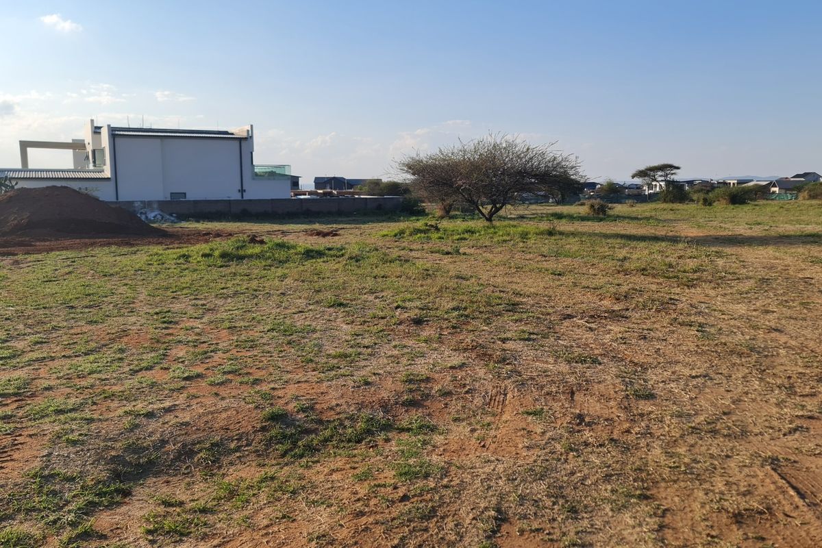 A view of a vacant residential plot of land with a boundary wall and surrounding neighborhood development.