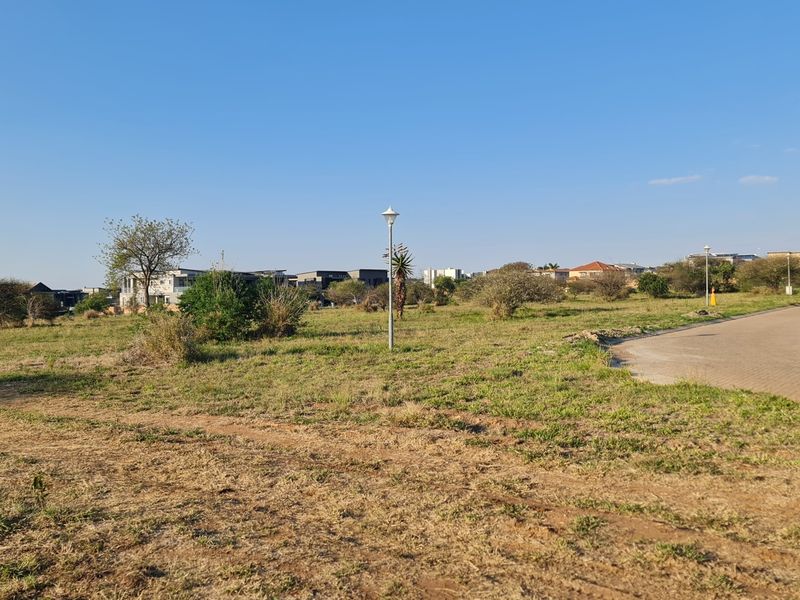 A vacant residential plot featuring established street lighting and access to a paved road in a developed neighborhood setting.