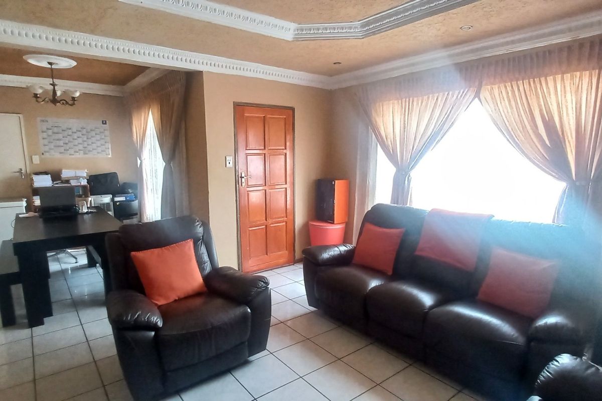 A living room featuring tiled flooring, decorative ceiling cornicing, and a timber panel door, offering a functional space with potential for modernization.