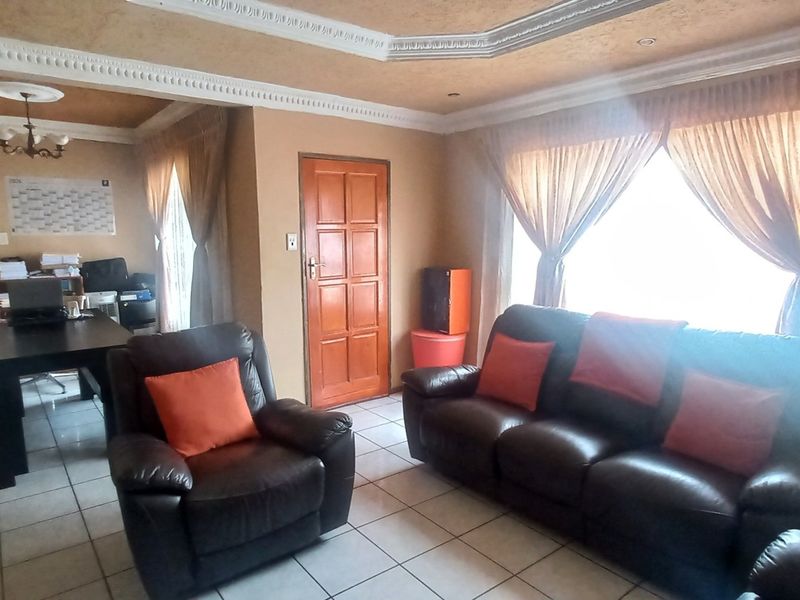 A living room featuring tiled flooring, decorative ceiling cornicing, and a timber panel door, offering a functional space with potential for modernization.