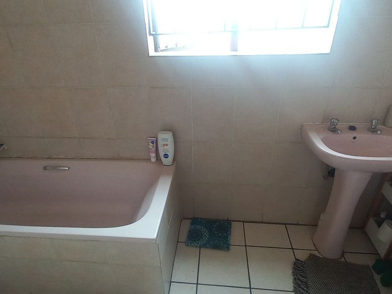 A functional bathroom featuring a built-in bathtub and a pedestal washbasin with neutral wall and floor tiling.
