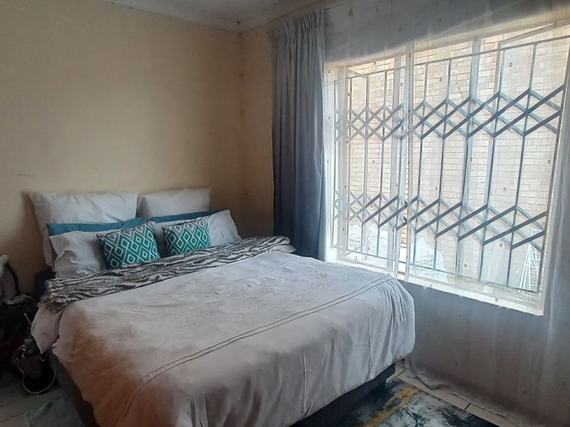 A standard bedroom featuring tiled flooring, a window with a fitted security gate, and neutral wall finishes.