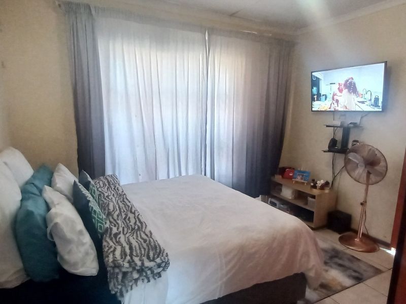 A standard bedroom featuring tiled flooring and wall-mounted television bracket, requiring cosmetic updates to wall finishes and general maintenance.