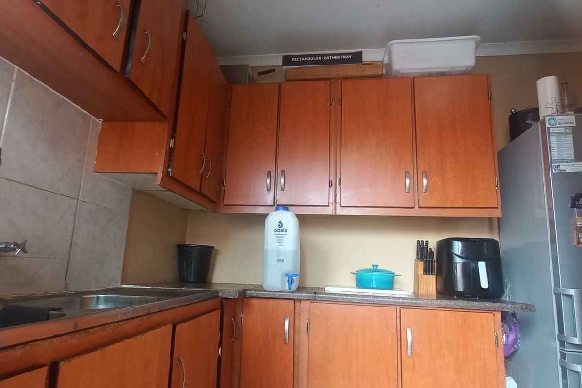 A compact kitchen featuring dated wooden cabinetry, laminate countertops, and a double stainless steel sink with tiled backsplash.