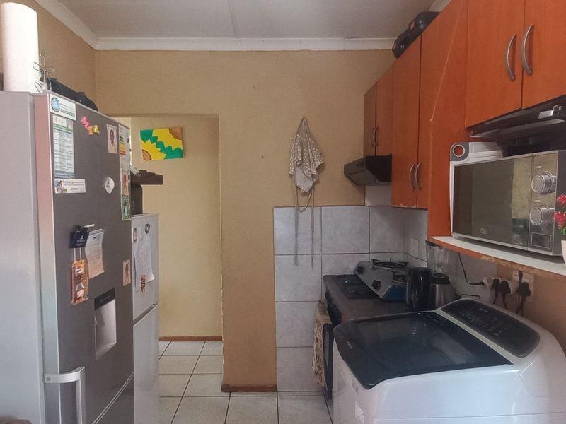 A compact kitchen featuring wooden cabinetry, tiled splashbacks, and tiled flooring, offering functional storage and preparation space in need of cosmetic updates.