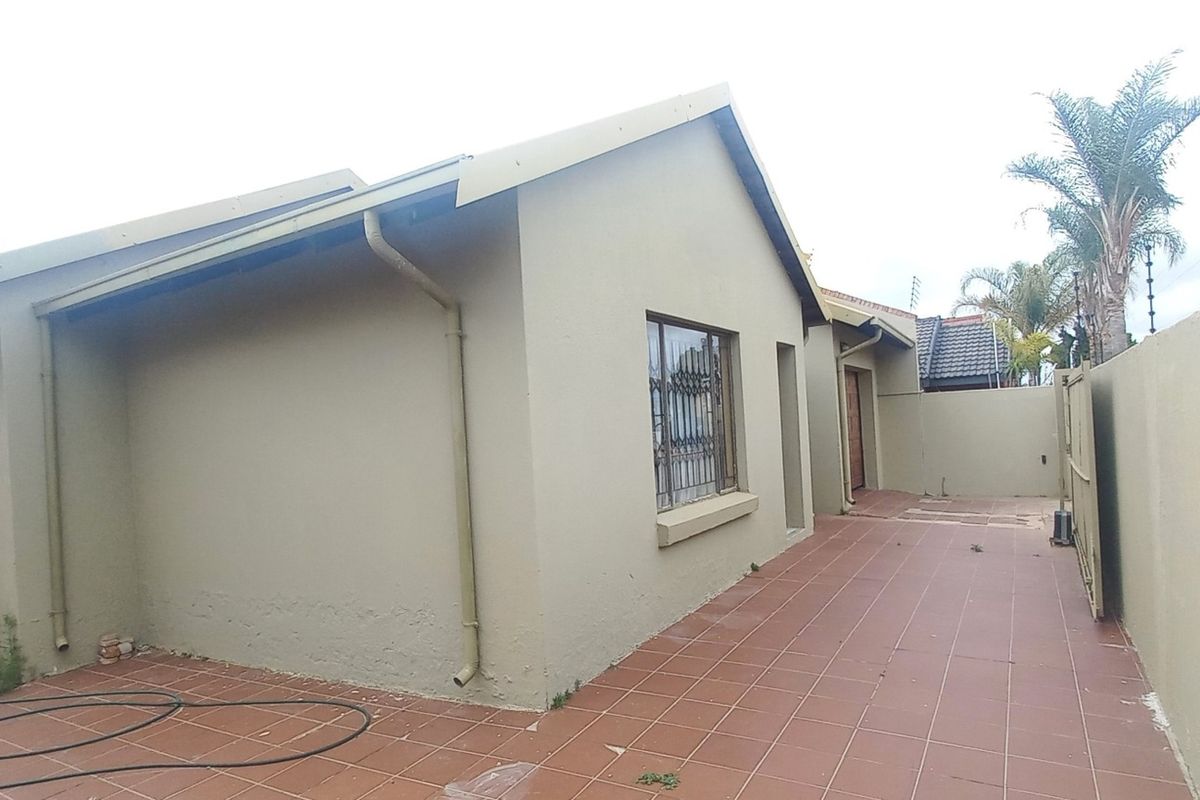 Rear exterior view of the house featuring a tiled patio area, perimeter wall with electric fencing, and security bars on the windows.