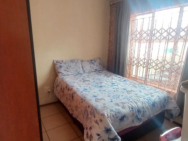 A standard bedroom featuring tiled flooring, a built-in wardrobe, and a window fitted with a security gate.