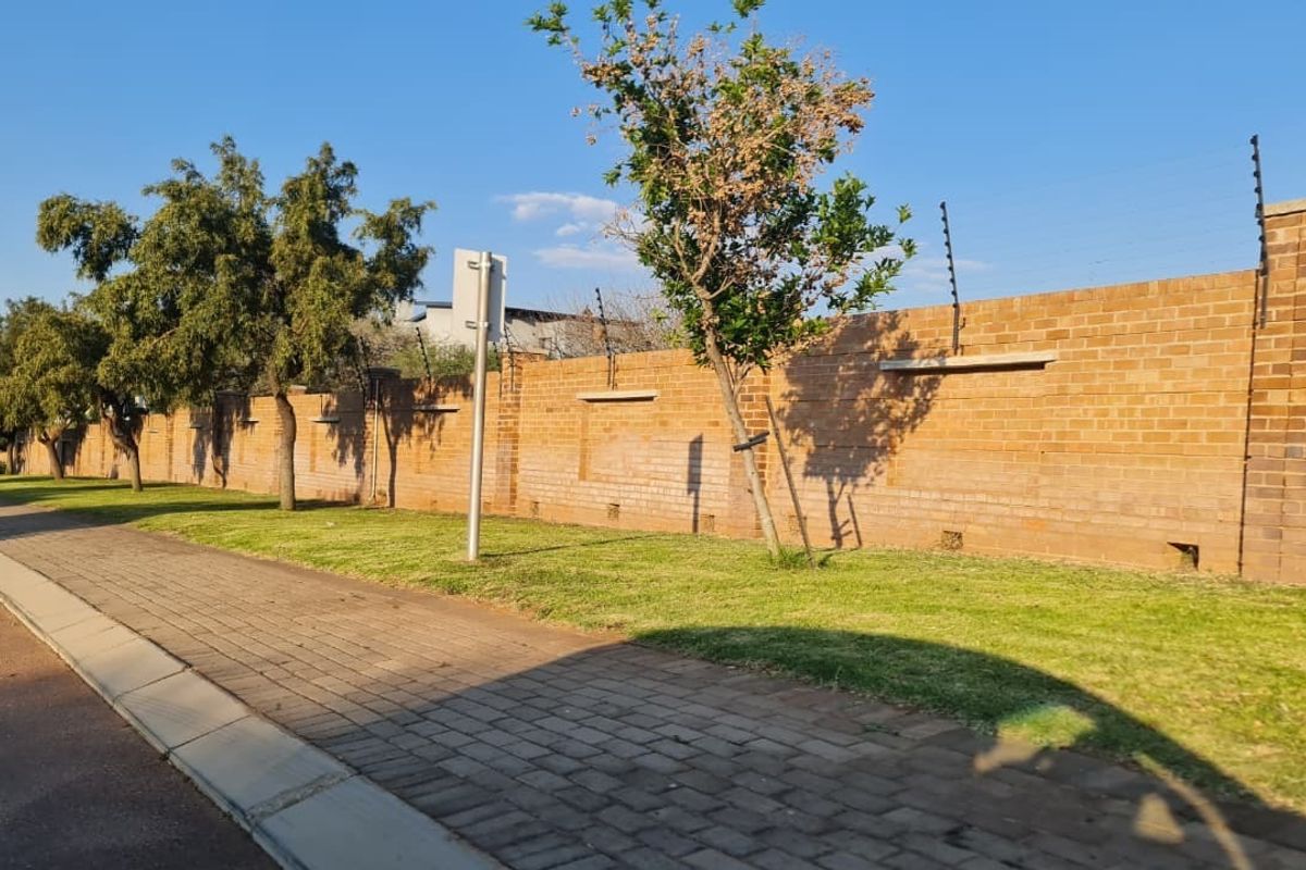 A view of the property's exterior brick boundary wall featuring integrated electric fencing, adjacent to a paved sidewalk and grass verge.